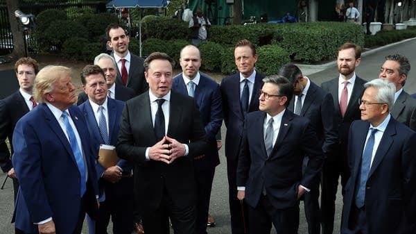A group of men in suits gathered outdoors, with photographers and onlookers in the background